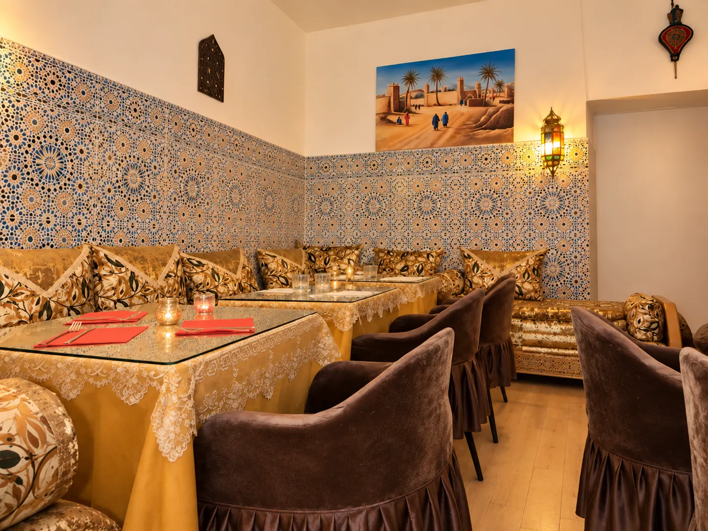 Salle dorée du restaurant : banquettes en zellige, coussins brodés et lanterne allumée